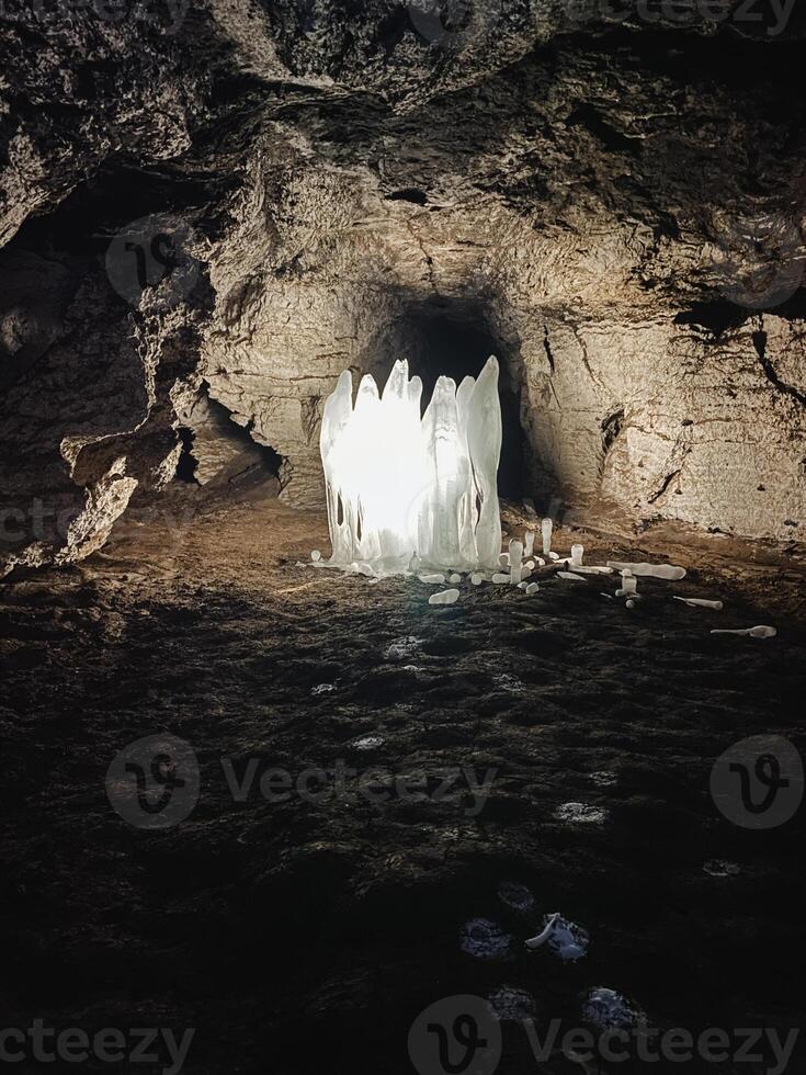 Inside the depths of a mysterious cave, one can find a vast and impressive ice formation that dominates the center of the space, creating a stunning natural spectacle in darkness photo