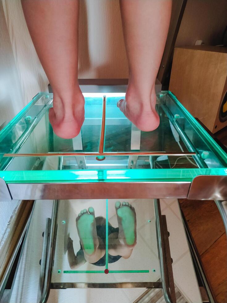 A person is currently having their feet meticulously measured while standing on a transparent glass platform that allows for precise readings and observations to be made photo