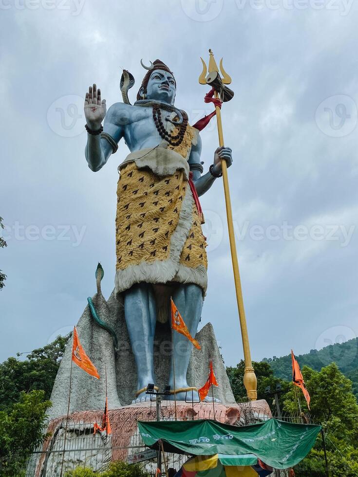 A remarkable large statue of a deity triumphantly holding a trident stands majestically, surrounded by the sky and clouds, surrounded by lush greenery, showcasing stunning art photo
