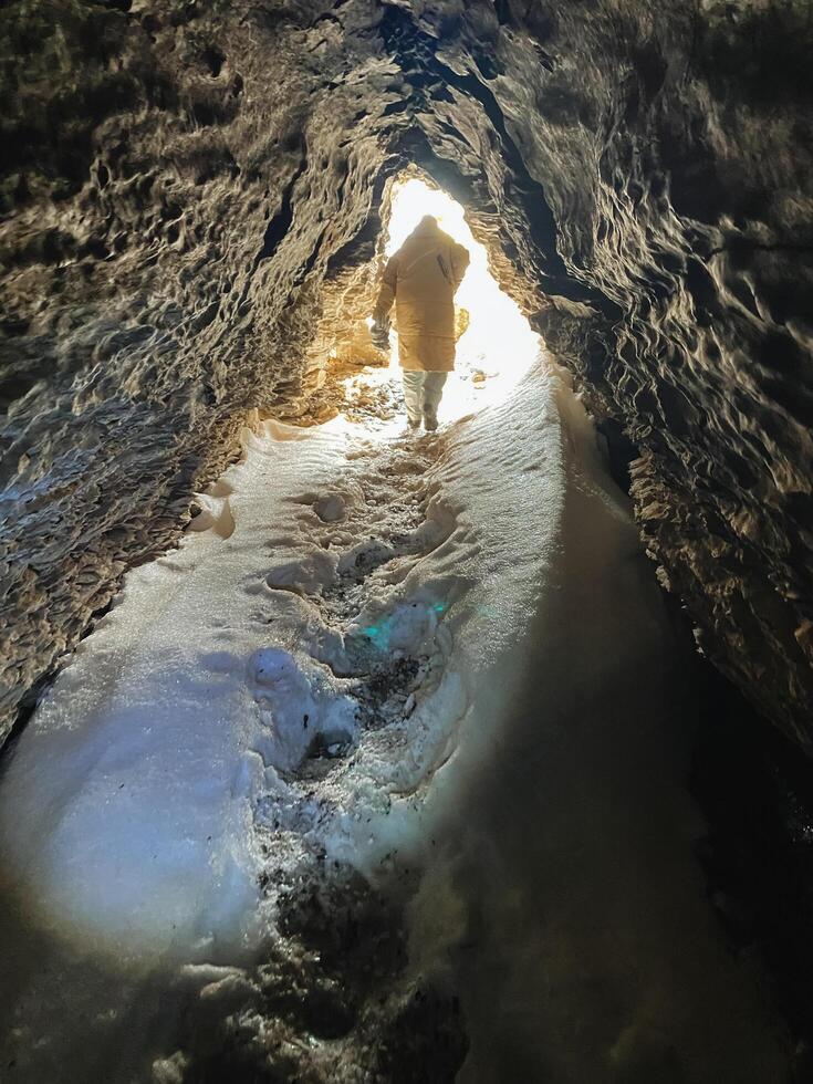 A solitary individual meticulously maneuvers through a dimly lit cave, wielding a powerful light, taking great care to find a secure path as they undertake this demanding expedition photo