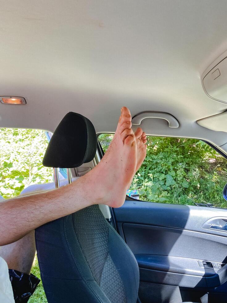 A person is comfortably seated in a car, fully relaxing with their feet propped up on the headrest, taking pleasure in their ride while enjoying the scenic view outside through the window photo