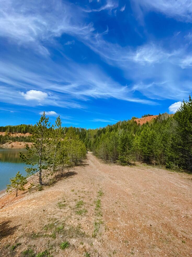 A long dirt road that winds its way toward a beautiful lake, which is elegantly surrounded by lush trees and greenery, creating a picturesque scene amidst natures beauty photo