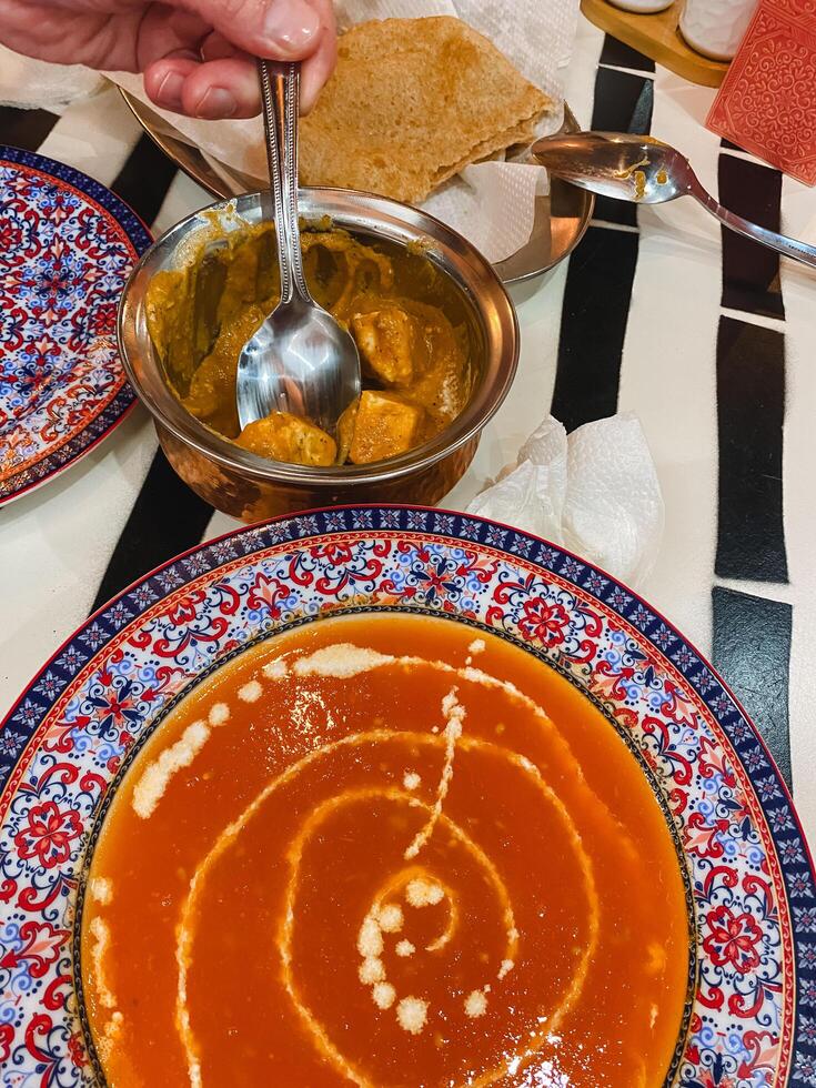 A person is carefully dipping a spoon into a bowl filled with delicious, steaming hot soup, enjoying the comforting aroma that wafts up from the dish, ready to savor each spoonful photo