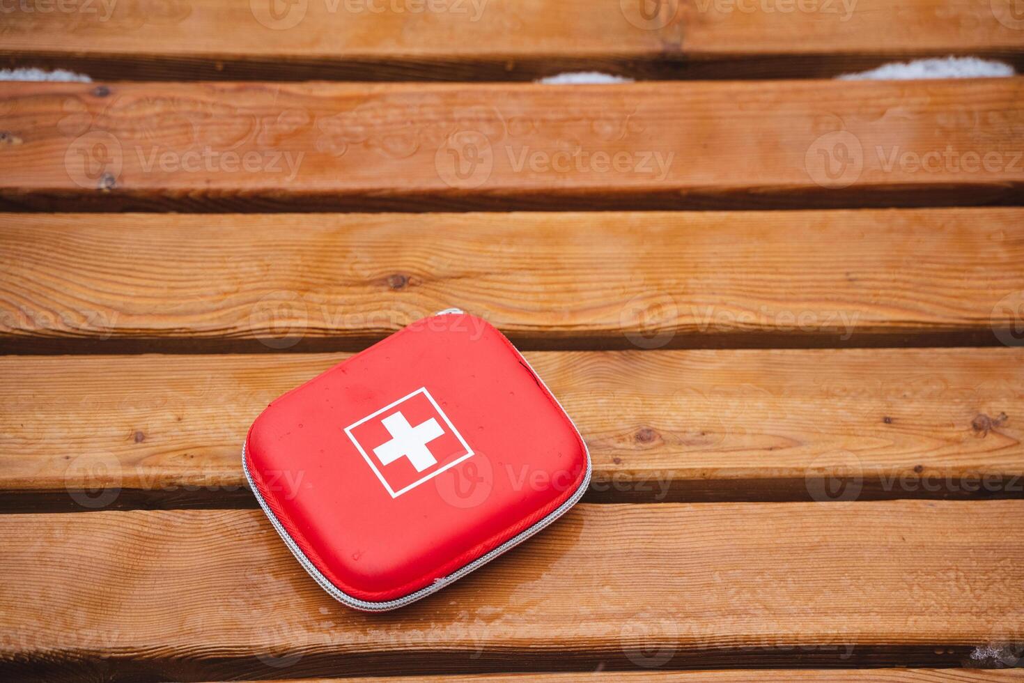 A Compact Red First Aid Kit is placed on a Wooden Surface, ready for use in various Emergency Situations that may arise during your outdoor activities or daily life routines photo