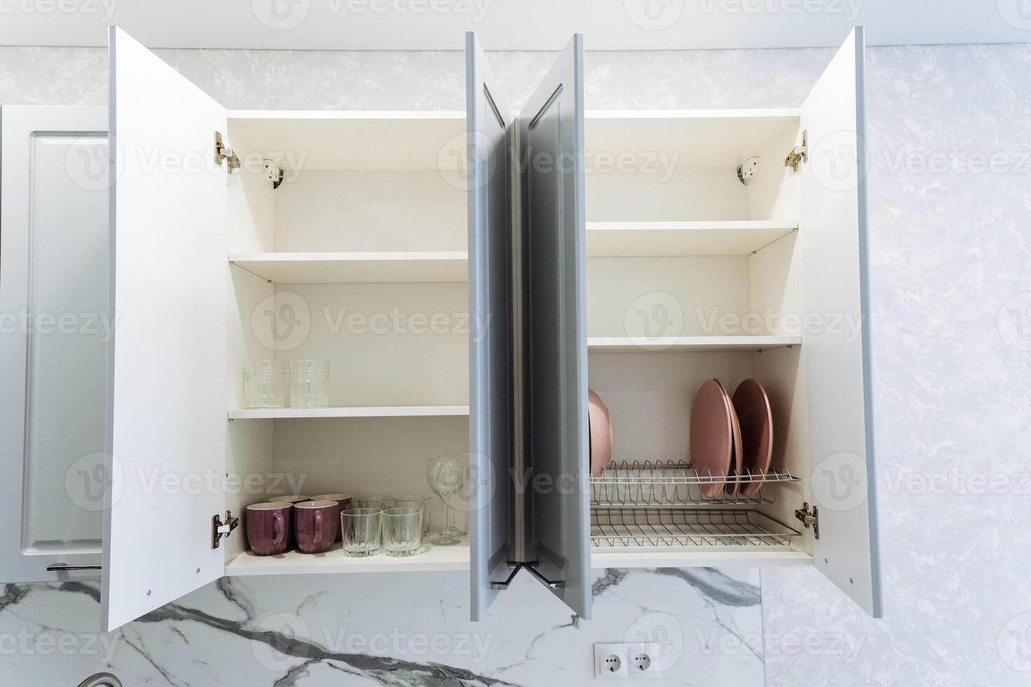 A kitchen cabinet featuring its doors wide open, showcasing a dish drying rack placed inside, indicating a space actively used for preparing meals and cleaning up afterward photo