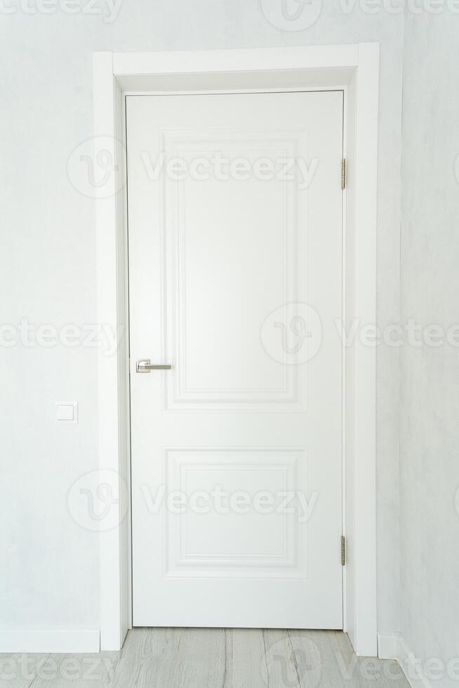 In a completely empty room characterized by white walls, there stands a white door that complements the wooden floor, creating a stark yet harmonious atmosphere for the space photo