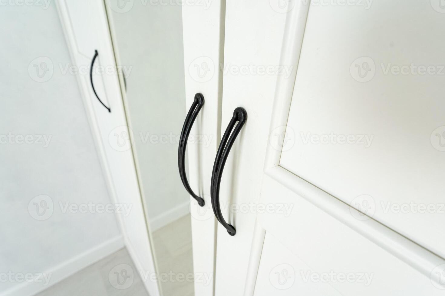 The image presents a closeup view of an elegant white wardrobe that features sleek, modern black handles along with a sizable attached mirror, enhancing both functionality and convenience photo