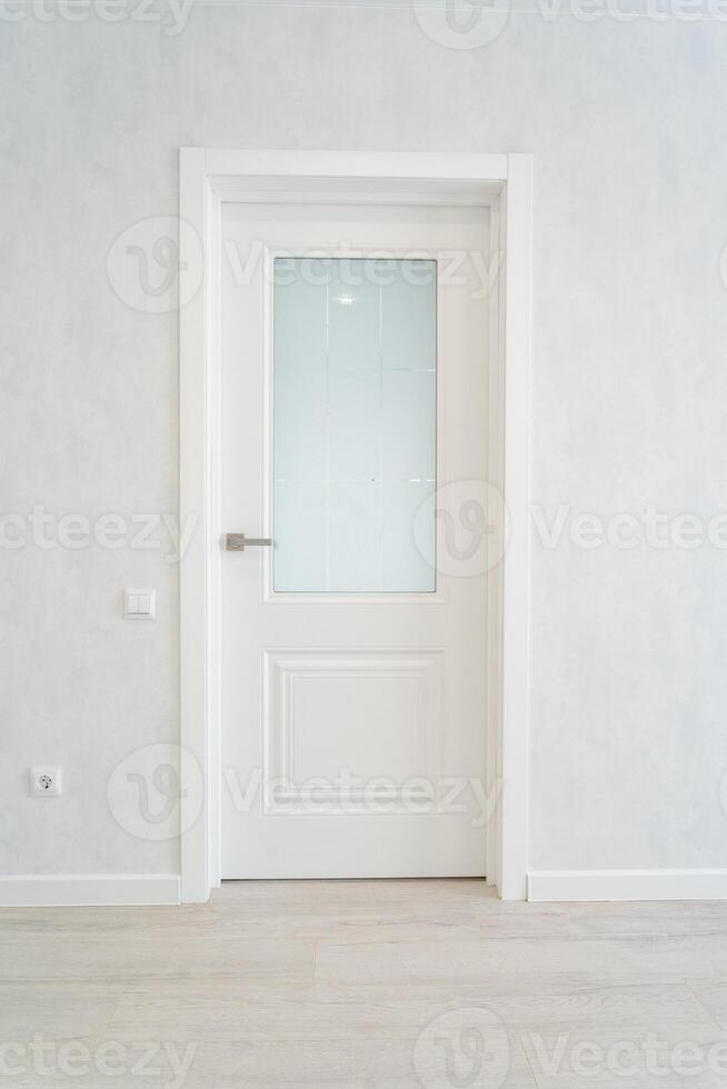 In an empty room, there stands a white door that features a glass window, adding a bit of natural light to the otherwise vacant space, enhancing the overall aesthetic of the area photo