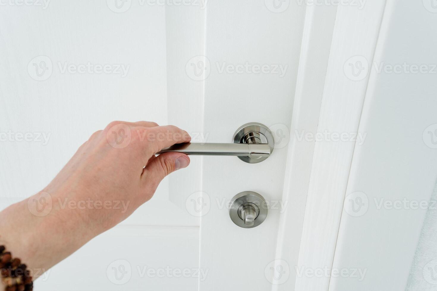The doorknob man holds it with his hand, the metal handle on the white door in the room, the fittings are their chrome. photo
