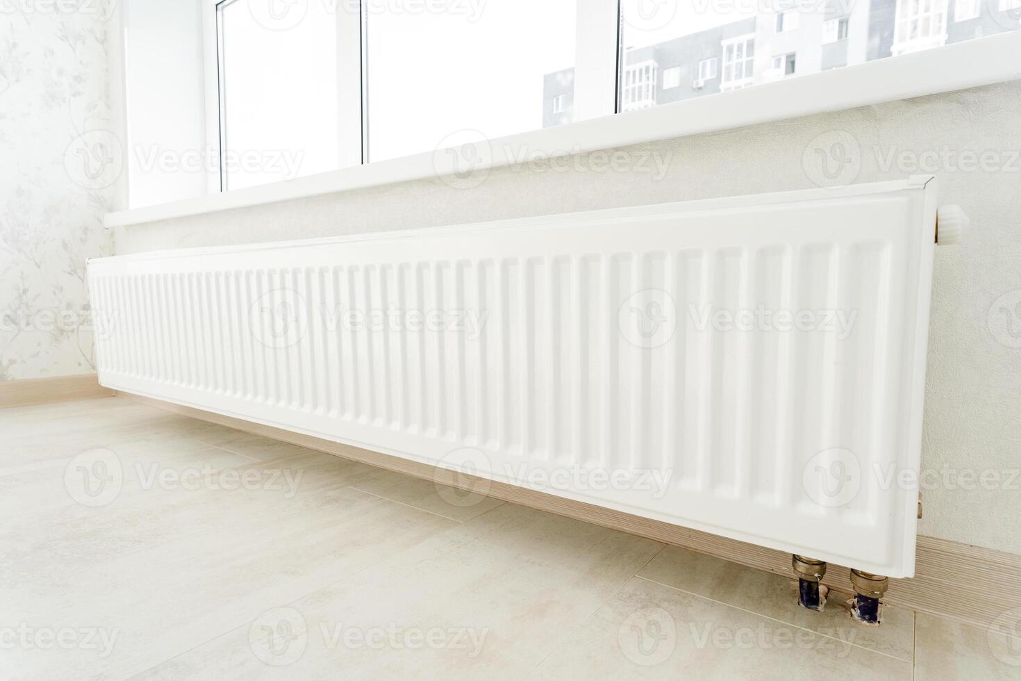 A white radiator sits next to a window in a room with hardwood flooring photo