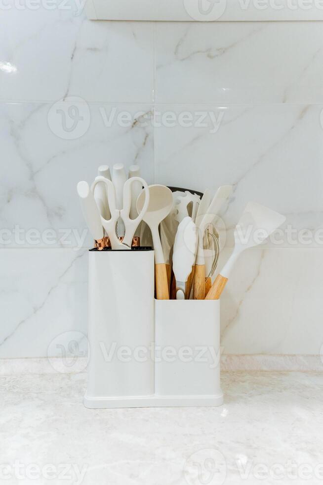 A white container that is filled to the brim with various kitchen utensils sitting prominently on a kitchen counter, ready for use and adding a splash of organization to the space photo