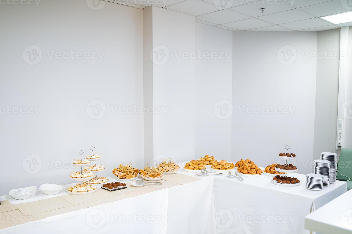 The room features a buffet table filled with a variety of food items, likely set up for an event. The decor includes wooden flooring, a rectangular table, and a ceiling above photo