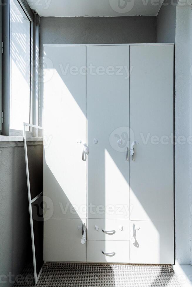 This cozy room features a large window for natural light, a stylish white wardrobe with drawers, and a generous mirror that adds aesthetic charm and practical functionality photo