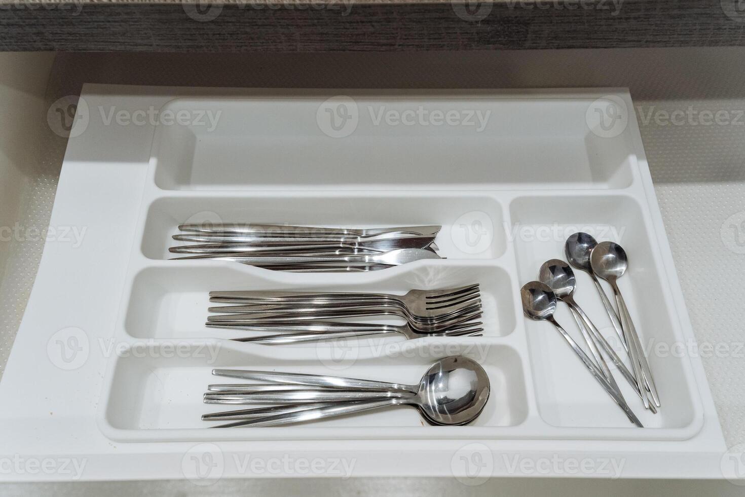 A white drawer that is completely filled with various types of silverware including forks, spoons, and even scissors, all organized neatly within the confines of the drawer photo