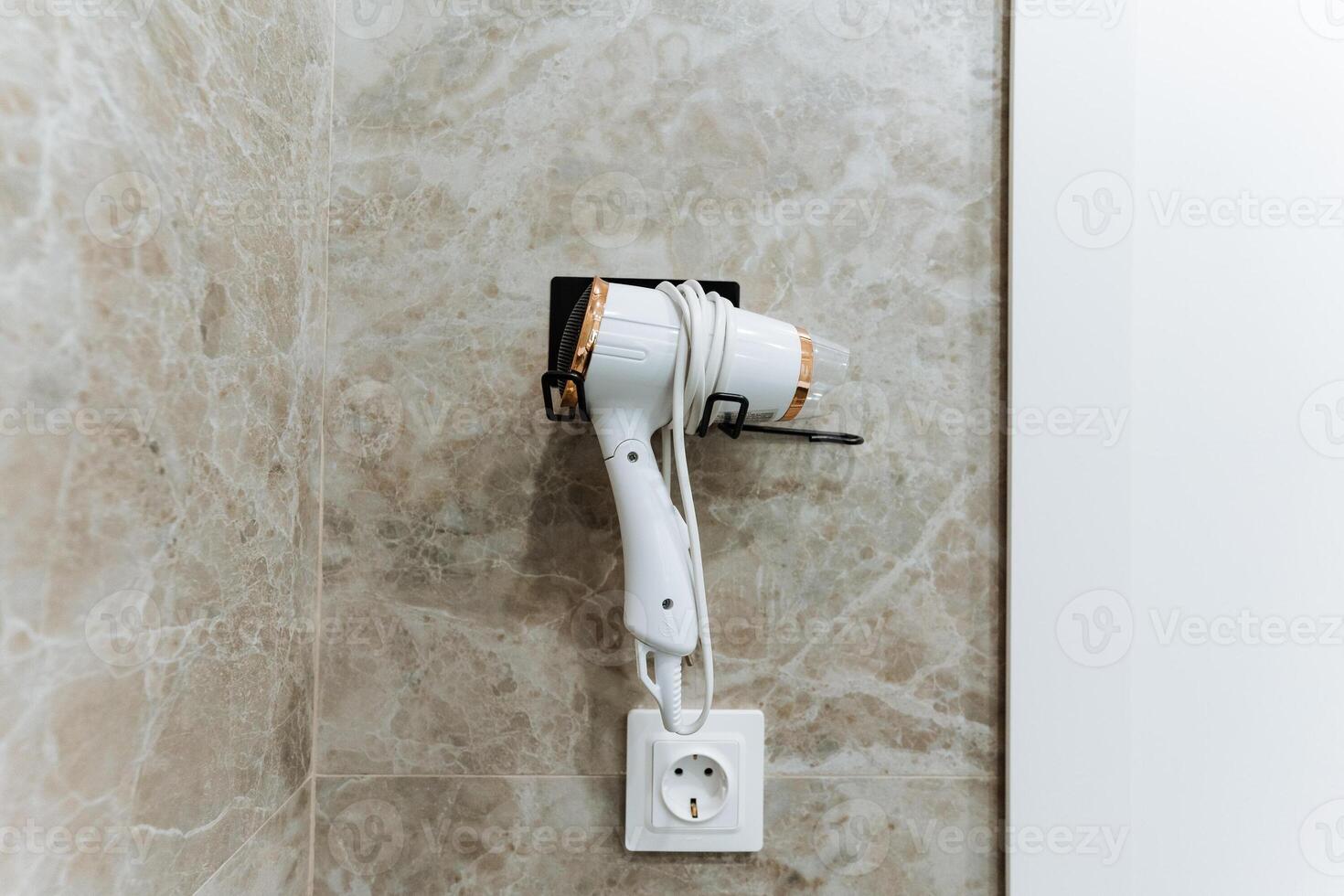 A hair dryer is currently hanging securely on a wall right next to an electrical socket, making it conveniently accessible for use whenever it is needed for drying hair or styling photo