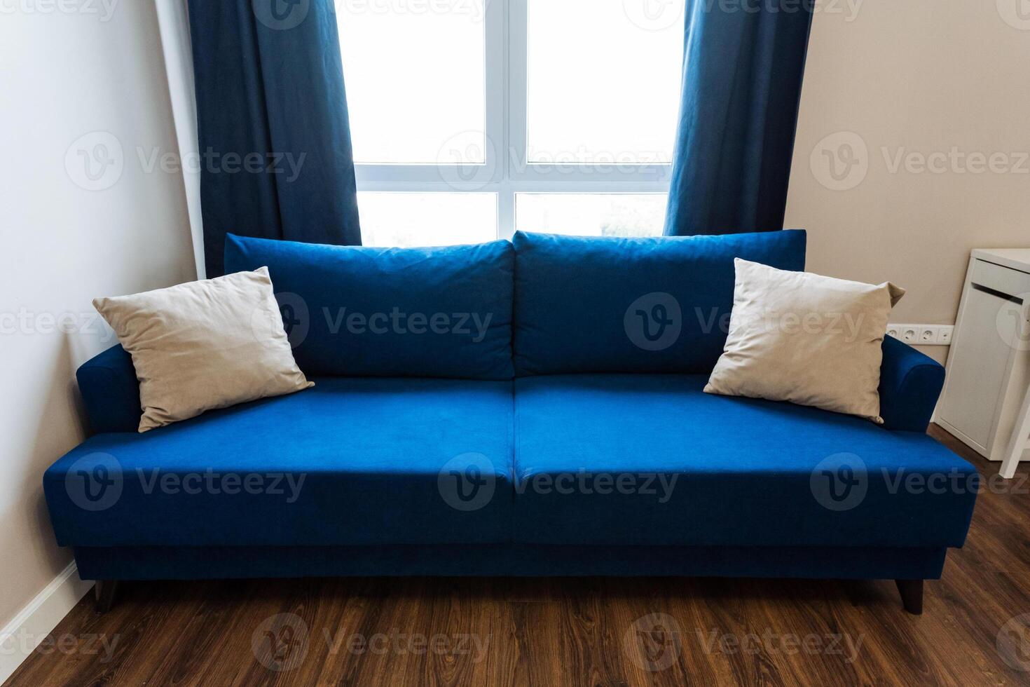 A cozy living room features an azure couch, white pillows, elegant furniture, hardwood flooring, and natural light, creating a stylish and comfortable space for relaxation and socializing photo