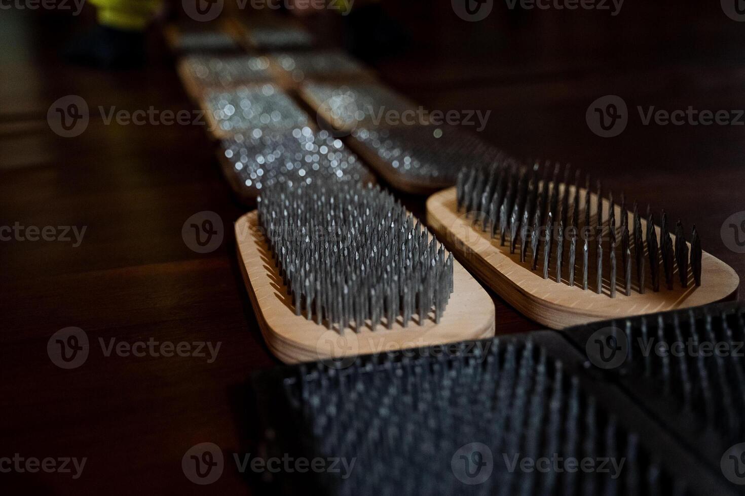 A long row of various wire brushes is neatly arranged on top of a sturdy wooden table, creating an interesting visual display that showcases essential tools for artists or musicians photo