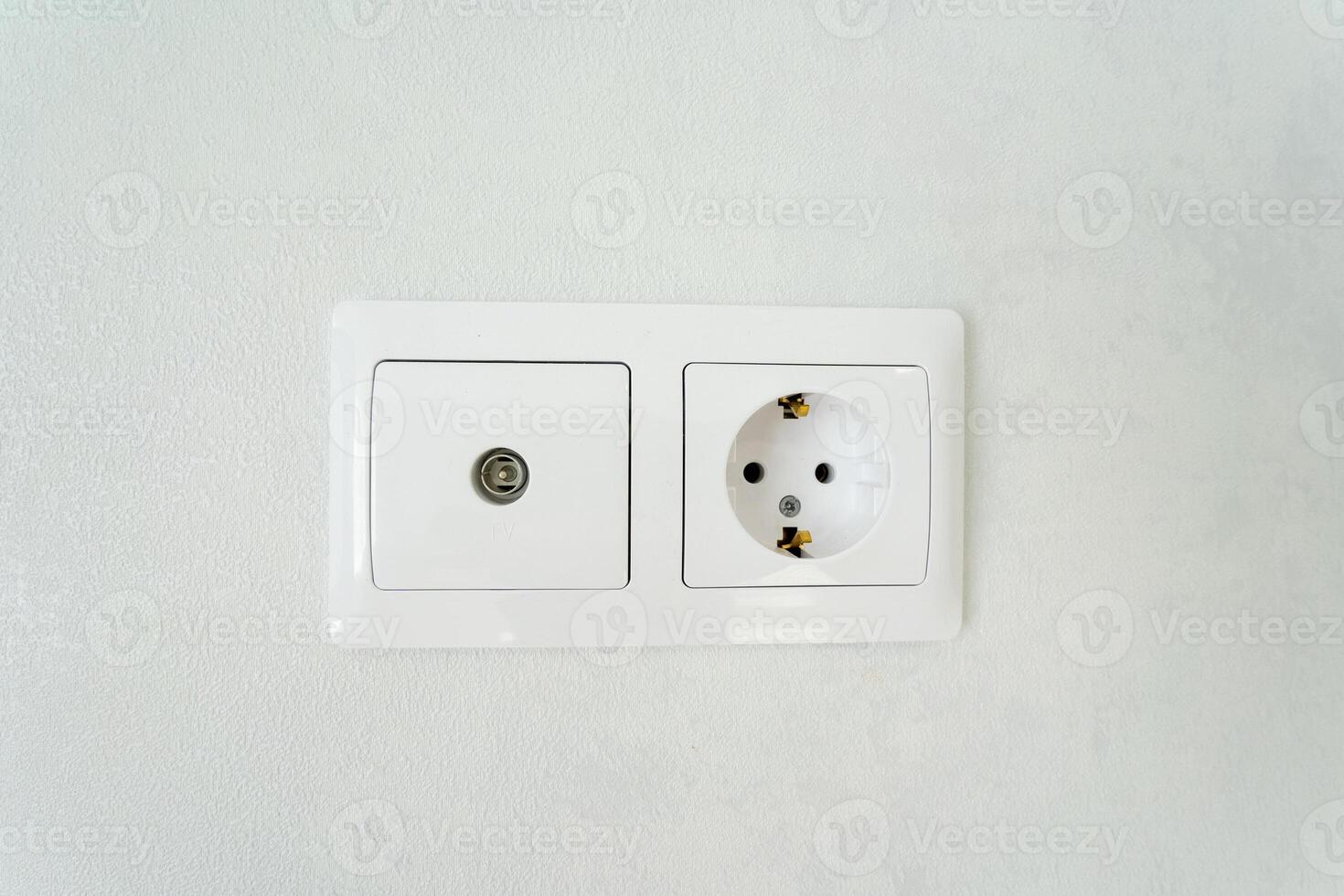 There is a plain white wall featuring a traditional electrical socket, along with a television antenna attached to it. This setup can be found in various rooms and serves several functions photo