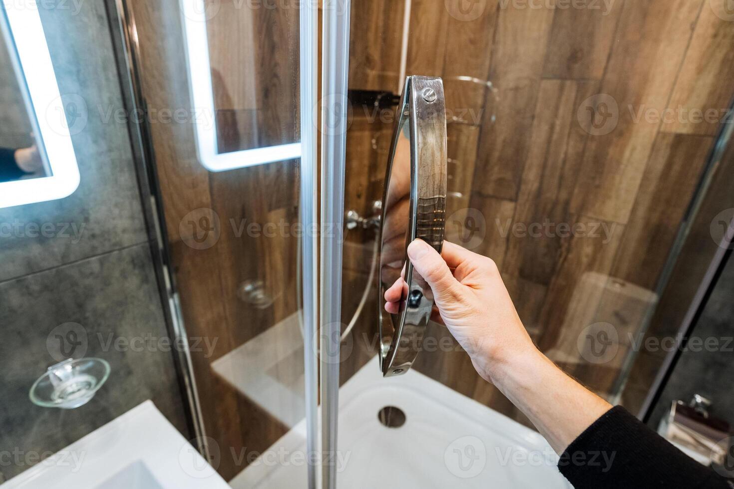 A person is gently opening the shower door in their bathroom, getting ready for a refreshing wash to kickstart their day or to relax and unwind after a long and tiring day photo