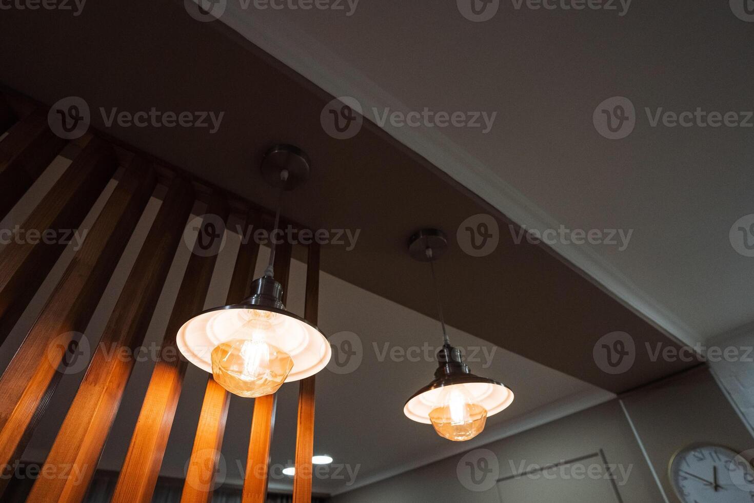In a room adorned with wooden accents and features, two decorative lights elegantly hang from the ceiling, situated conveniently near a ticking clock that adds to the ambiance photo