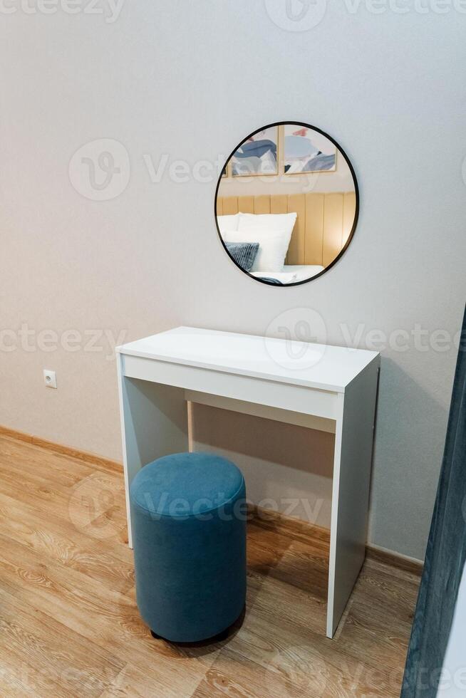 The beautifully designed bedroom includes a chic vanity with an elegant mirror for sophistication and a cozy blue ottoman that enhances aesthetic appeal and invites comfort photo