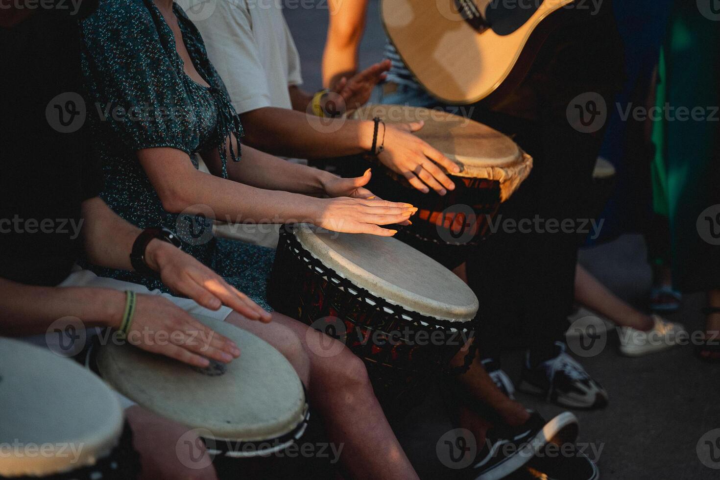 A lively group of people are enthusiastically playing drums while a talented man skillfully plays a guitar, creating an energetic atmosphere filled with delightful music and entertainment photo