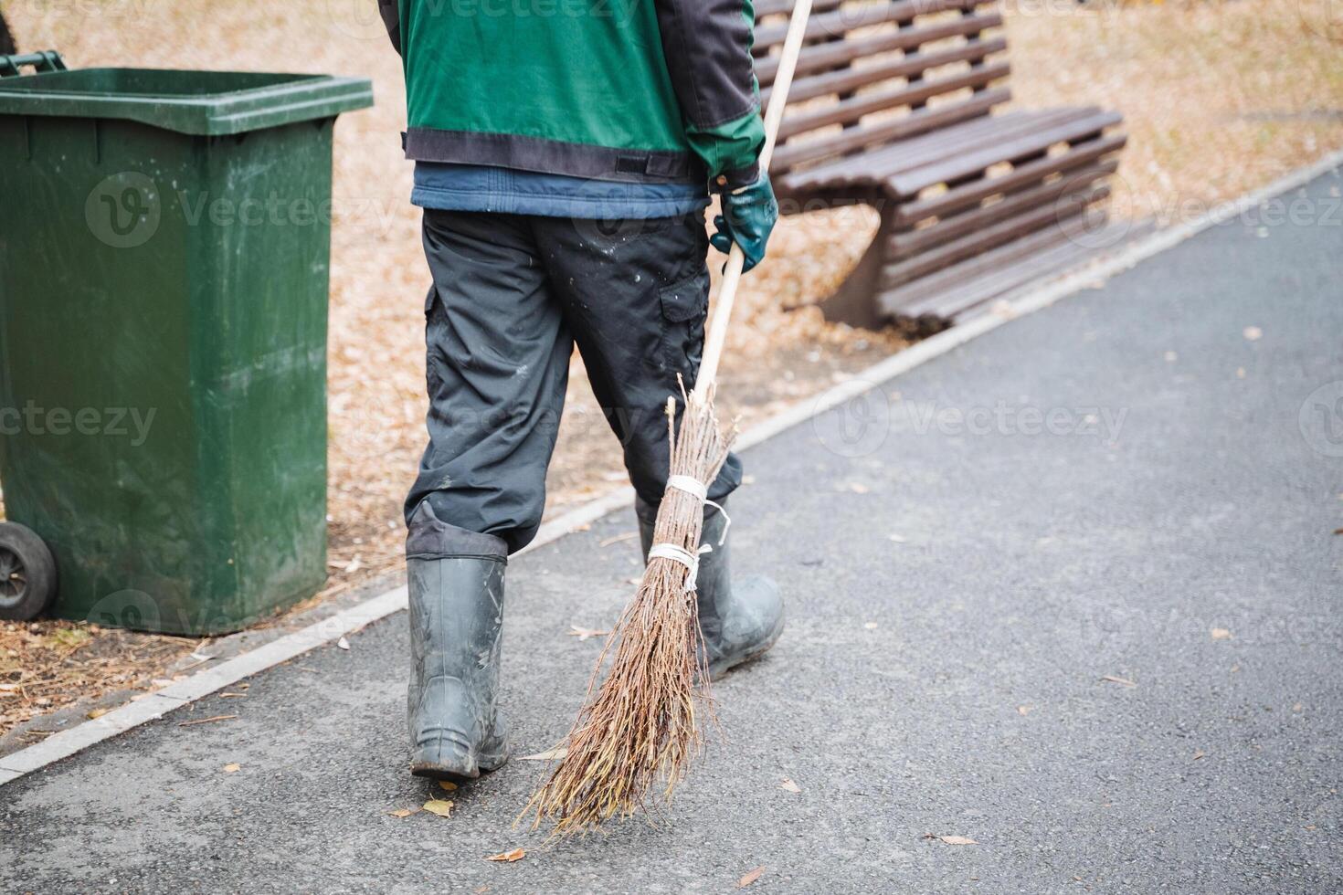 A man is casually strolling down a meticulously maintained sidewalk, gripping a broom firmly in his hand, prepared to clean up any debris or litter that may have accumulated along his path photo