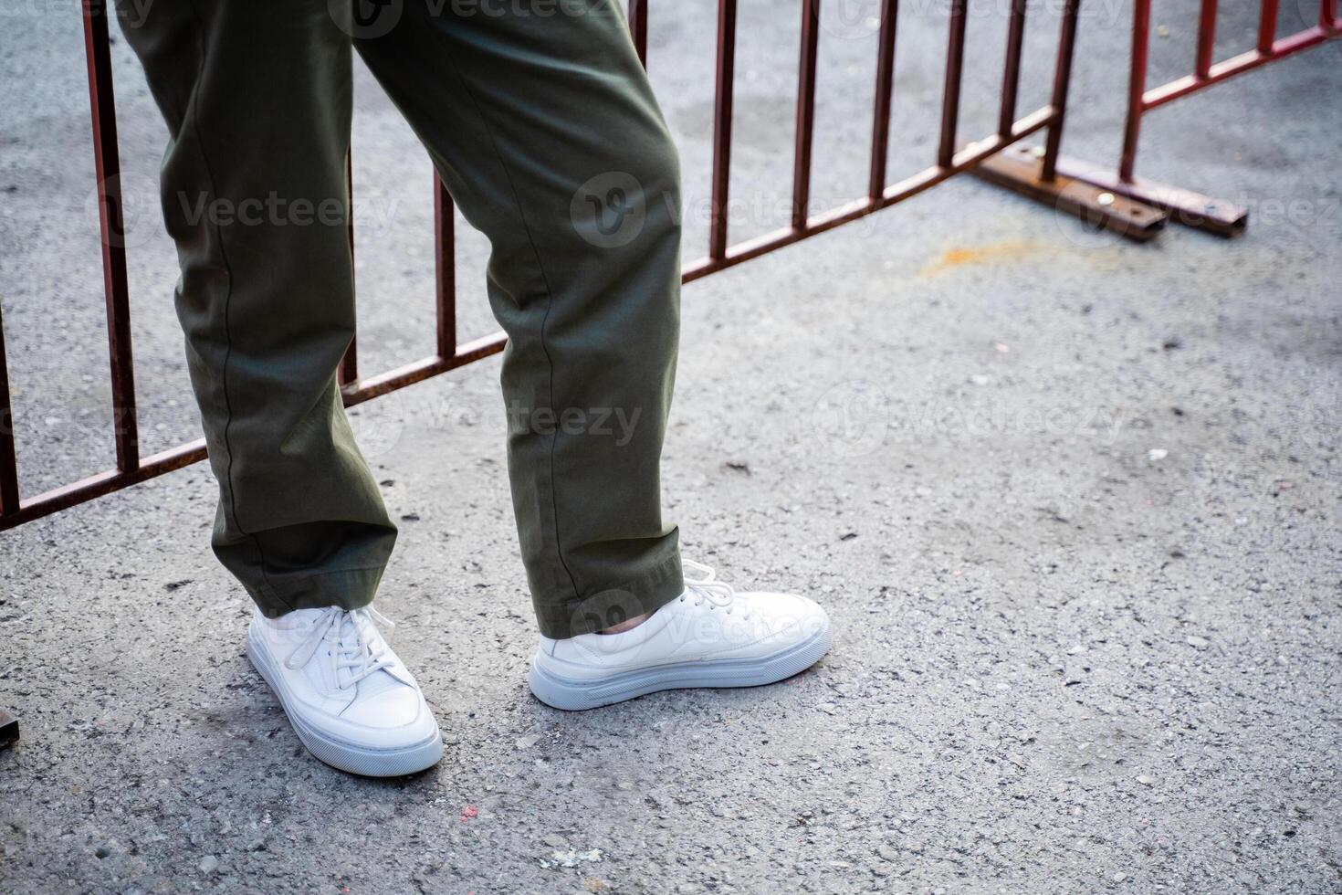 There is an individual who is dressed in white shoes and is currently positioned in front of a wooden fence, creating a visible contrast against the background of asphalt photo