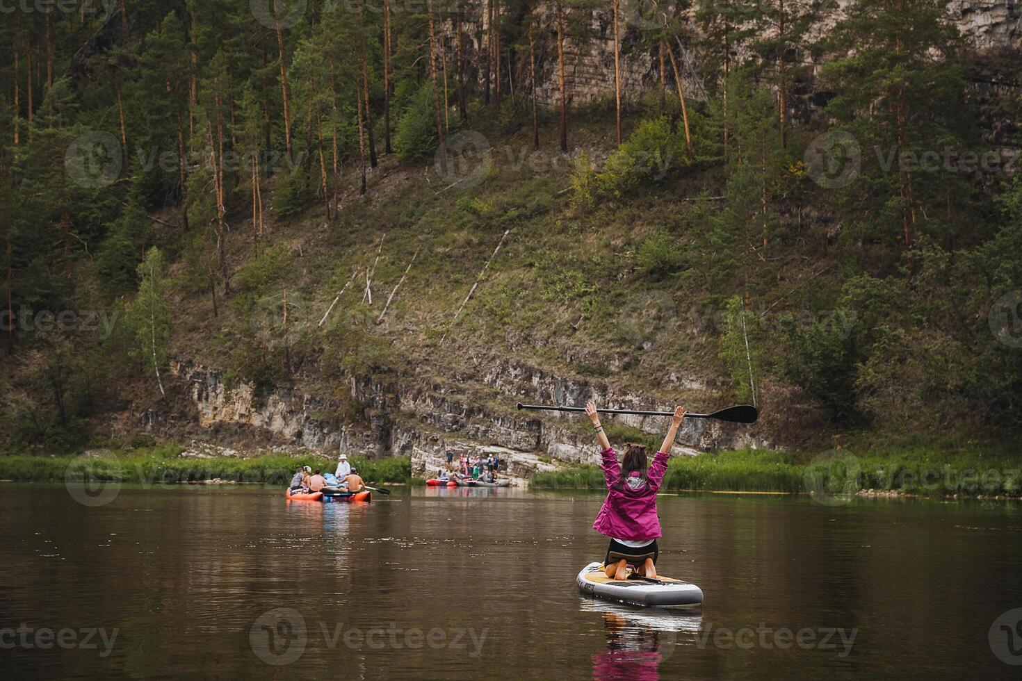 A confident person skillfully balances on a paddle board in the serene and calm waters, taking in the beauty of a lovely day that is filled with lush greenery and vibrant flowers all around photo