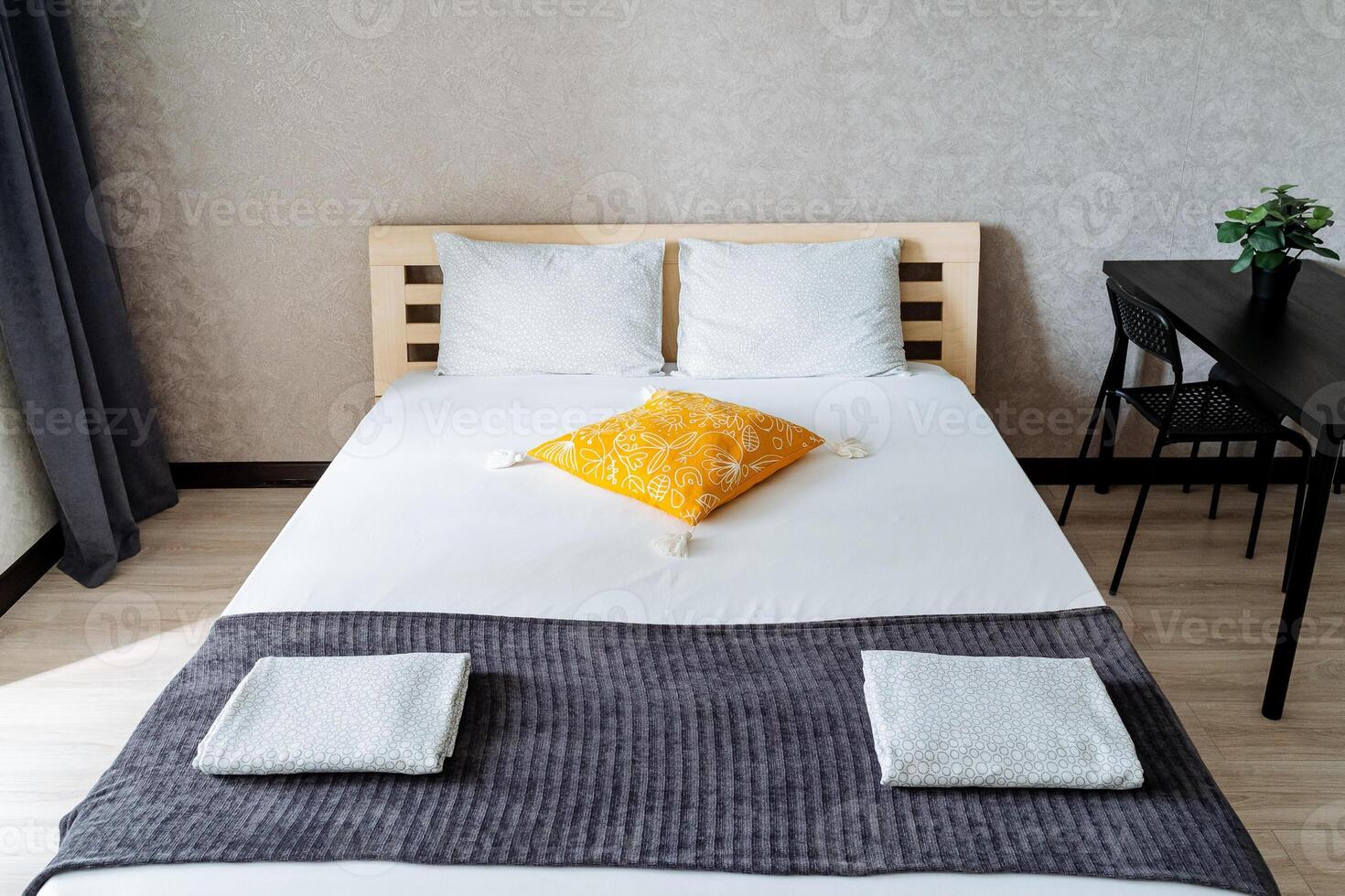 In a cozy bedroom, there is a beautifully arranged bed adorned with a vibrant yellow pillow, adding a cheerful touch to the overall decor of the room, making it feel inviting and warm photo