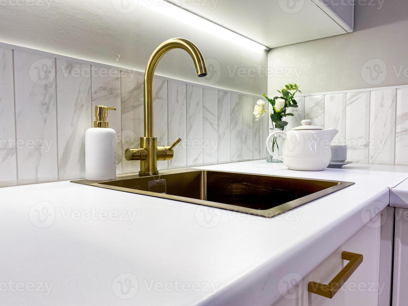 In a welldesigned kitchen, there is a lovely kitchen sink that features a luxurious gold faucet accompanied by a convenient soap dispenser elegantly placed on the countertop photo