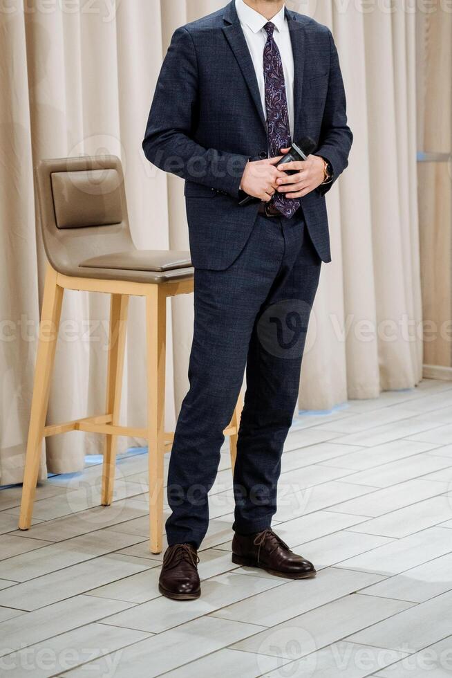 A welldressed man wearing a formal suit and a stylish tie is standing beside a chair, presenting an elegant and polished appearance that is appropriate for various formal occasions photo