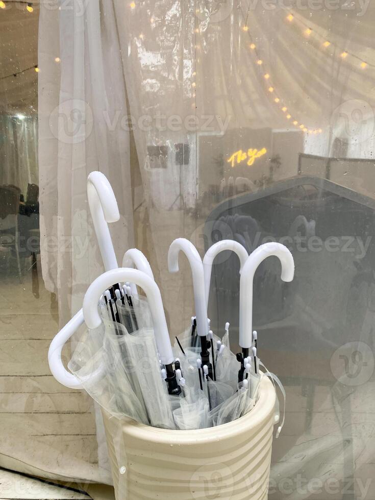 In front of a large window, there is a bucket filled to the brim with clear umbrellas, perfectly arranged and ready for use, creating a striking visual element in the room photo