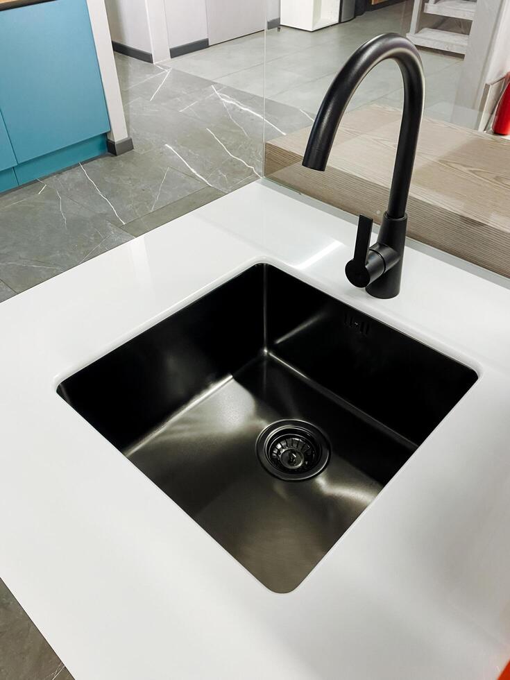 In a modern kitchen, there is a striking black sink paired with a sleek black faucet that sits elegantly atop a pristine white countertop. This design enhances the overall aesthetic photo