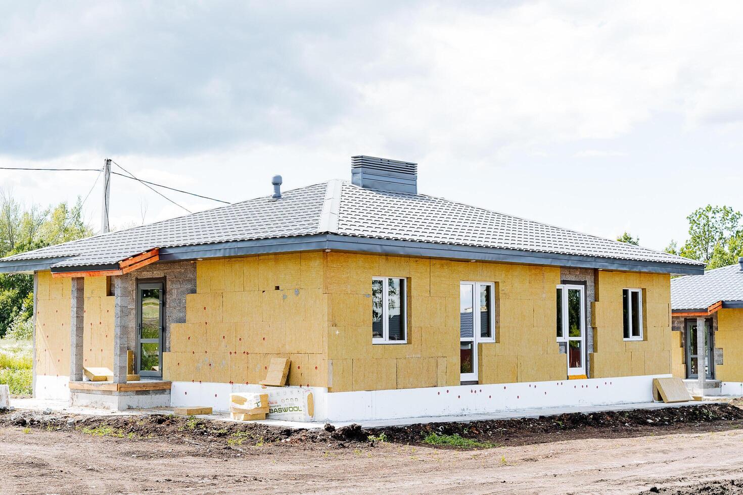 A bright yellow house is currently under construction in a large dirt field, surrounded by the elements of nature and the anticipation of future developments in the area photo