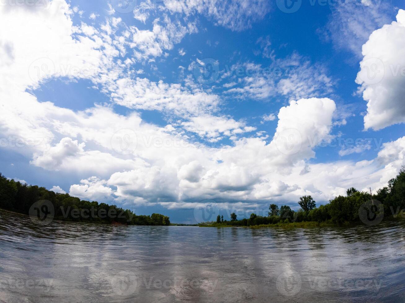 A serene and tranquil lake, beautifully surrounded by vibrant green trees, mirrors fluffy white clouds floating in a bright blue sky, creating a stunning and picturesque natural landscape photo