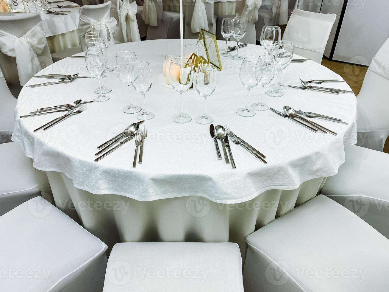 A beautifully arranged round table featuring pristine white linens and polished silverware is perfectly set up and ready for a delightful wedding reception event to gracefully unfold photo