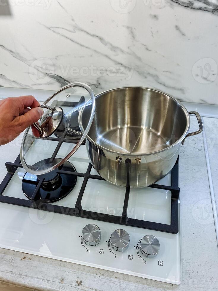In a wellequipped kitchen for culinary creativity, a person holds a pot lid over a stove, ready to check or add ingredients, showcasing the art of cooking and food preparation photo