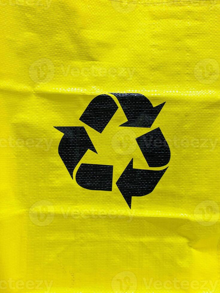This vibrant yellow bag features a bold black recycling symbol, highlighting its ecofriendly design that positively impacts the environment and promotes responsible consumption photo