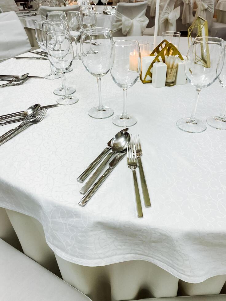 A beautifully arranged white table cloth which is elegantly set with silverware and sparkling wine glasses placed gracefully on top of it, creating an inviting dining atmosphere photo