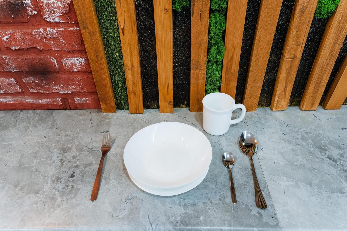 On a charming table positioned in front of a rustic wooden fence, there lies a beautifully arranged dining set consisting of a plate, a cup, spoons, and a fork, creating a delightful scene photo