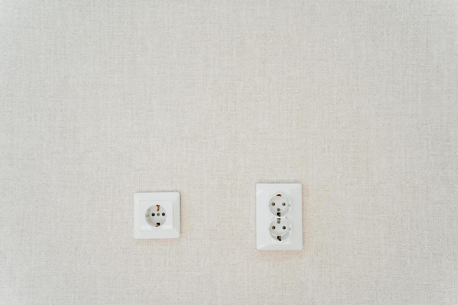 Two white wall sockets shaped like rectangles hang on the white wall photo