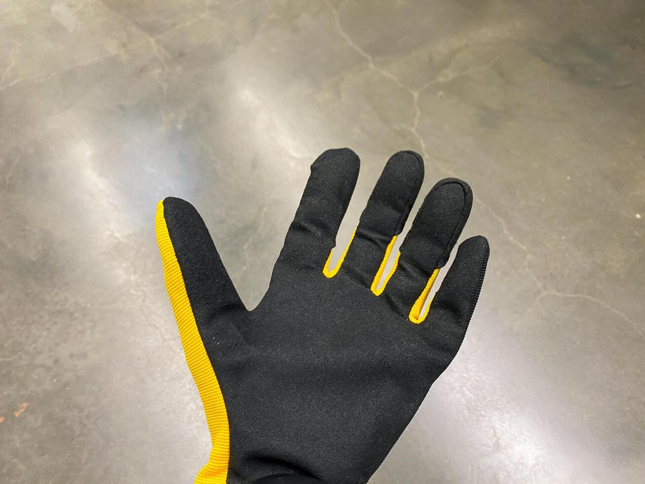 This image presents a closeup view of a Black and Yellow Work Glove resting on a rough and textured concrete surface, showcasing its unique design and intricate details photo