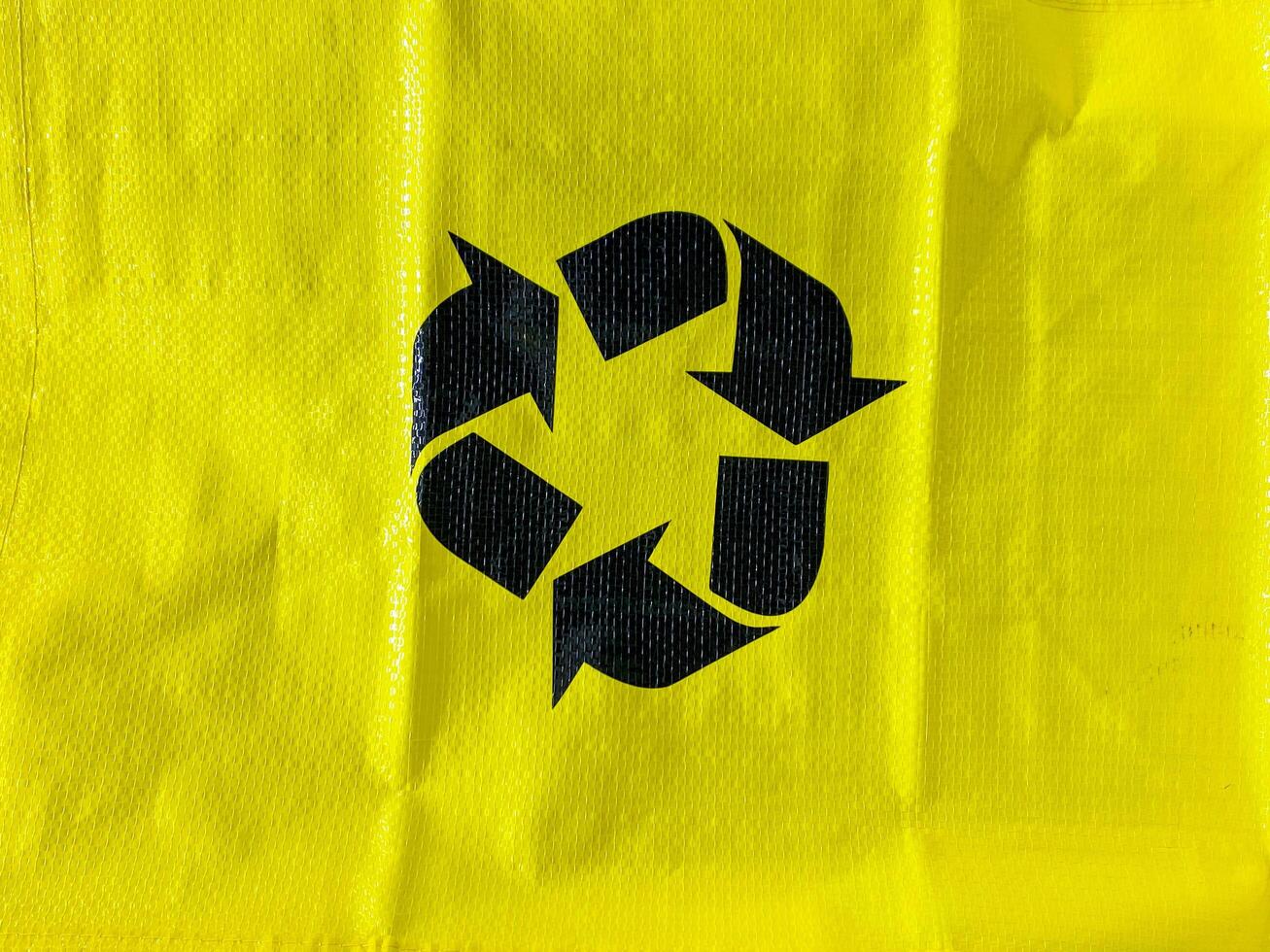 The item in question is a vibrant yellow bag that features a bold black recycling symbol prominently displayed upon its surface, indicating its environmental significance photo