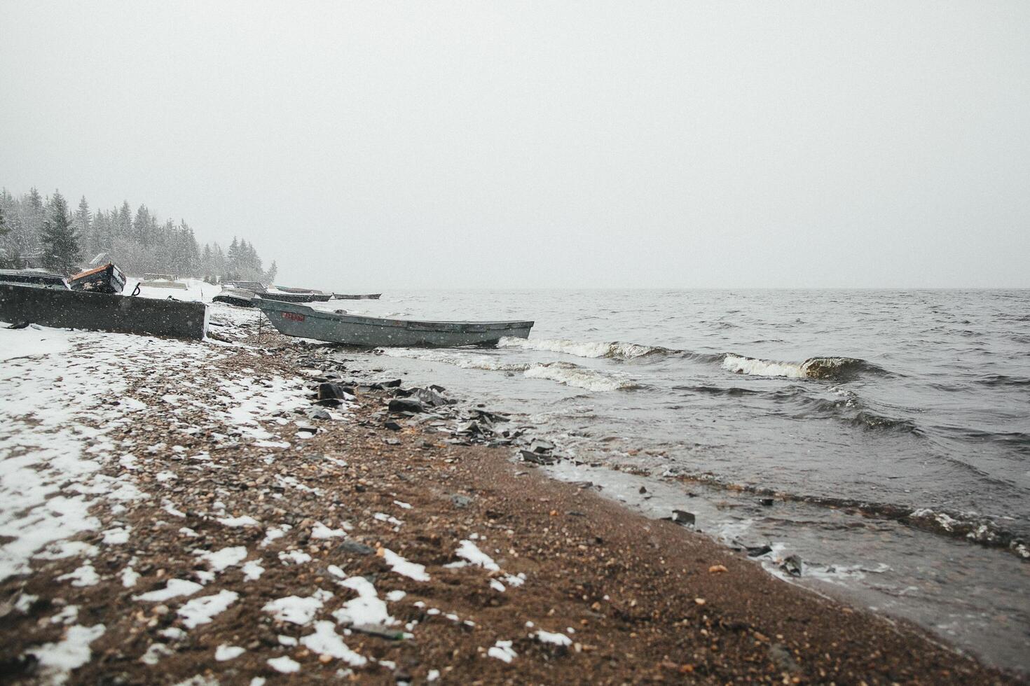 A Snowy Beach With Boats In The Water And Trees In The Background photo