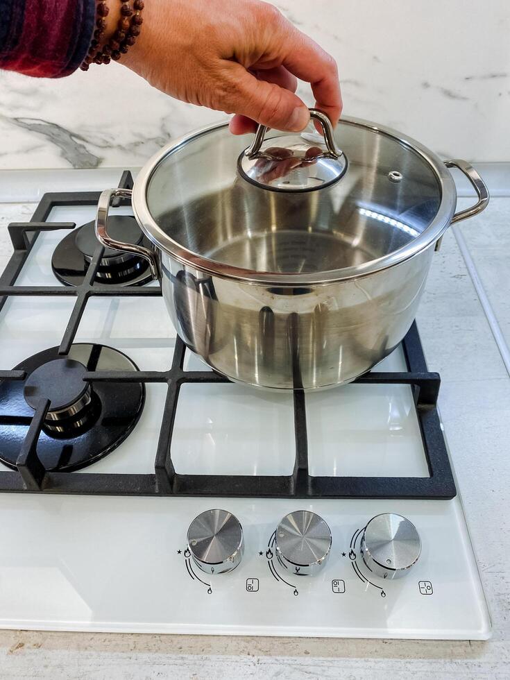 A skilled chef is carefully hand placing the lid on a shiny stainless steel pot positioned on a modern gas stove, preparing a delicious meal photo