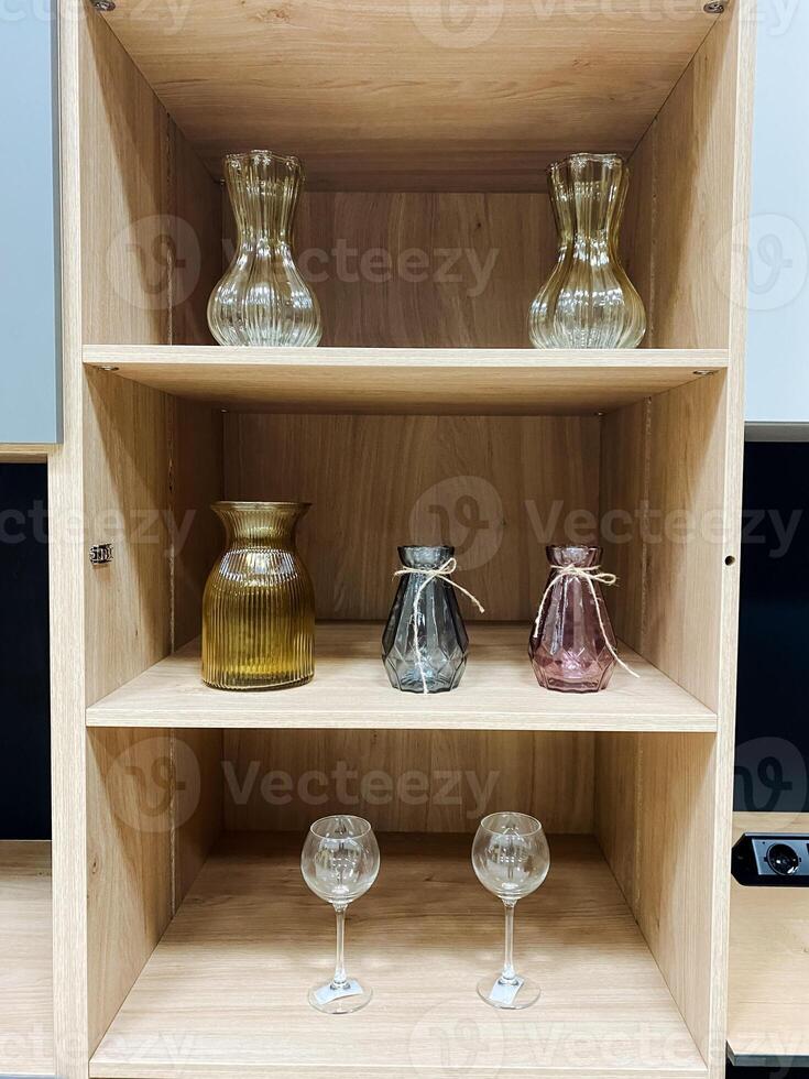 A beautifully crafted wooden shelf elegantly showcases an array of stunning vases accompanied by a delightful assortment of fine wine glasses that are arranged artfully across its surfaces photo