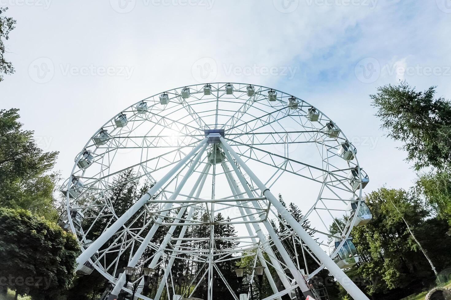 In the heart of the park, there is a large ferris wheel surrounded by green trees. This setting combines nature, fun, and relaxation in a perfect blend of amusement and natural beauty photo
