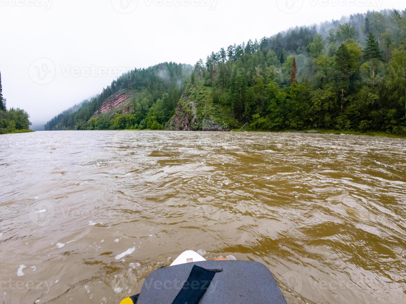 A brightcolored kayak is peacefully floating on a serene river, with majestic mountains towering in the background, creating a stunning natural landscape that captivates the view photo