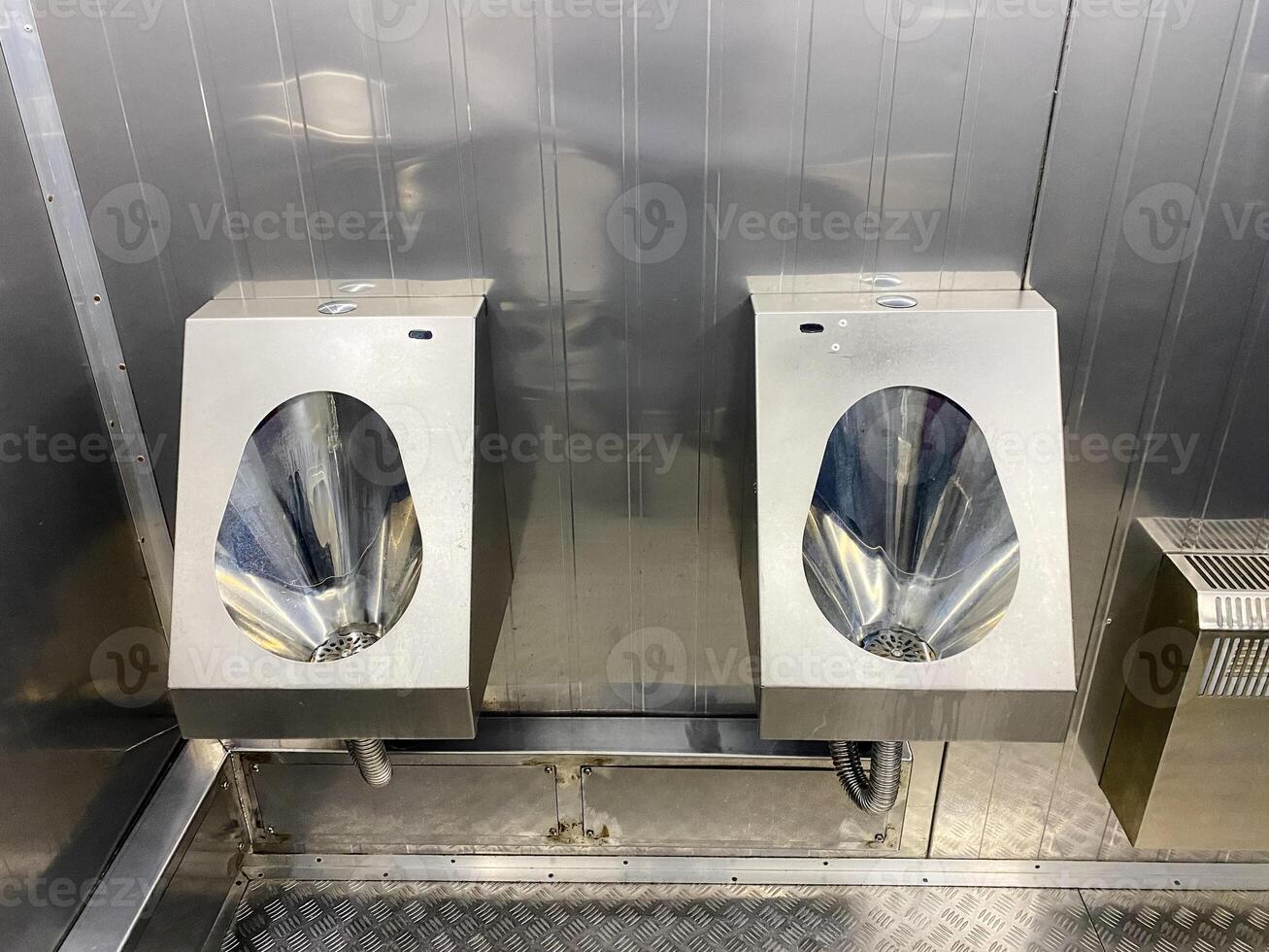 Two stainless steel urinals are side by side in a bathroom photo